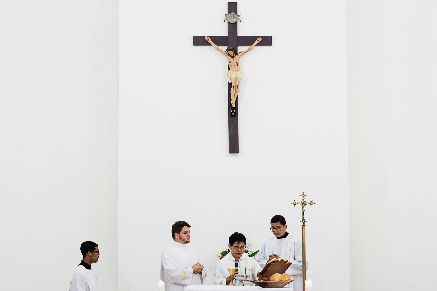 Priests conducting a religious ceremony inside a church under a large crucifix.