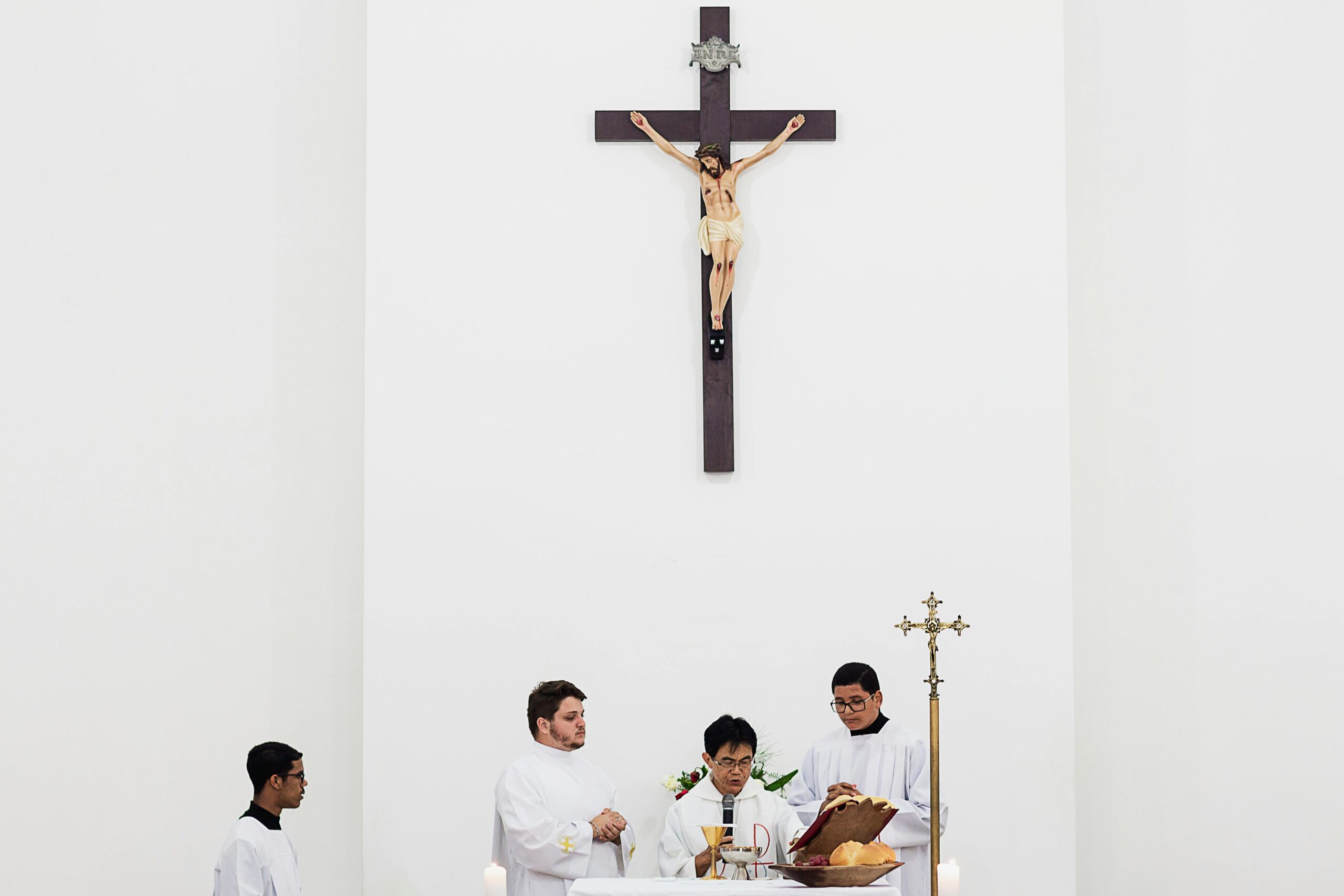 Priests conducting a religious ceremony inside a church under a large crucifix.