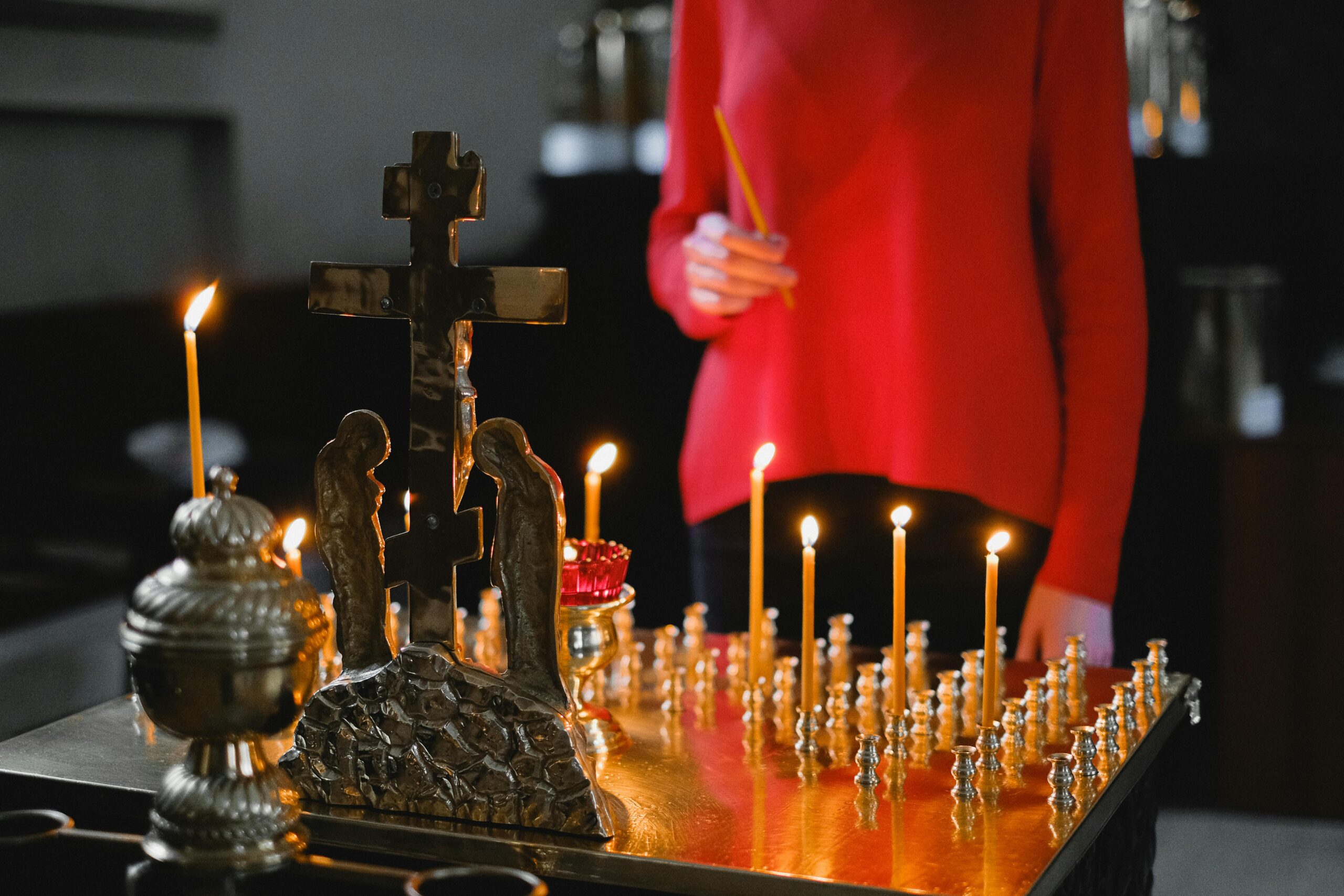 A woman lighting candles at an Orthodox altar with cross and statues in a church.